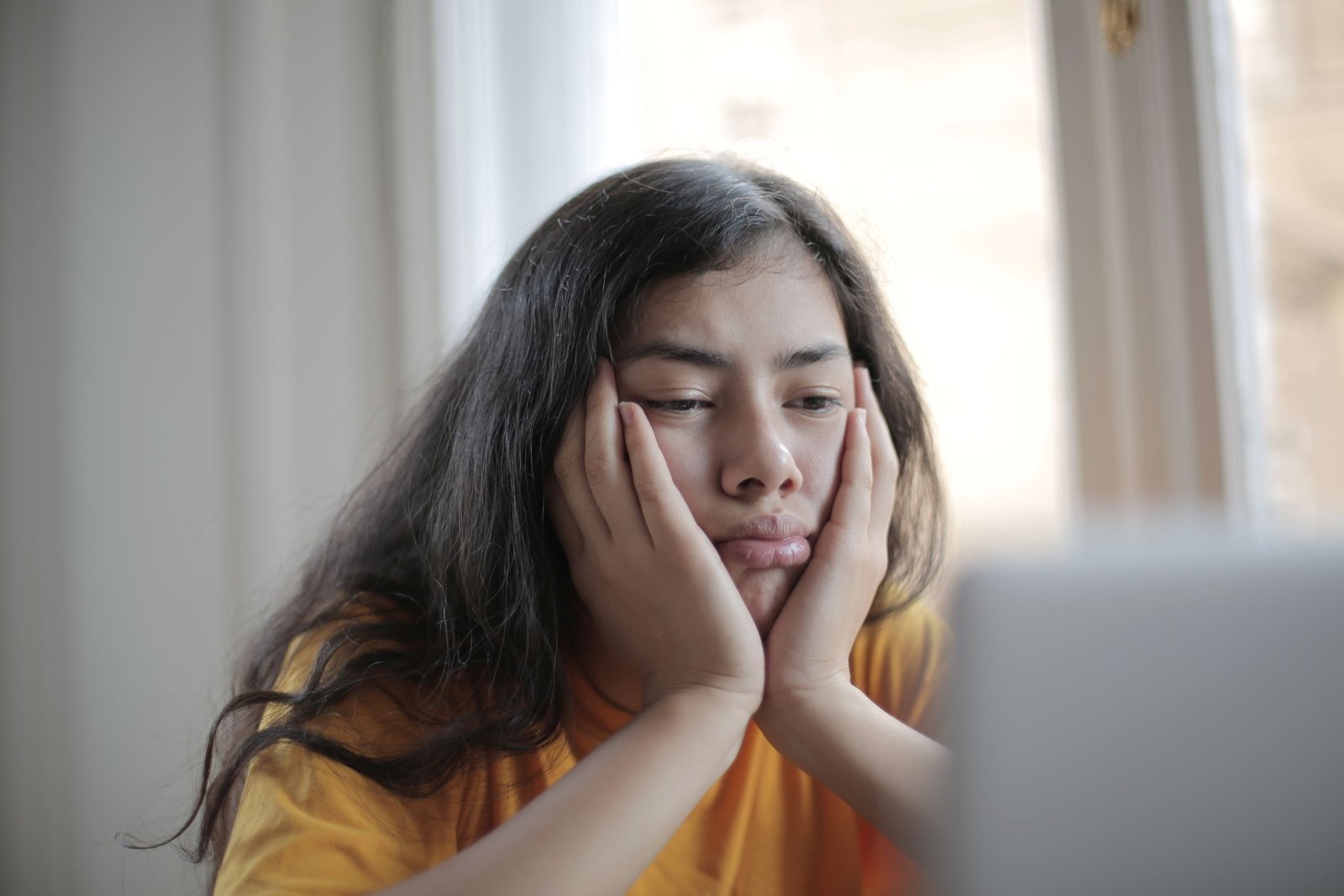 Performance Review Demotivated. Bored ethnic female in casual clothes sitting at table with netbook and watching sad movie while resting at home during weekend