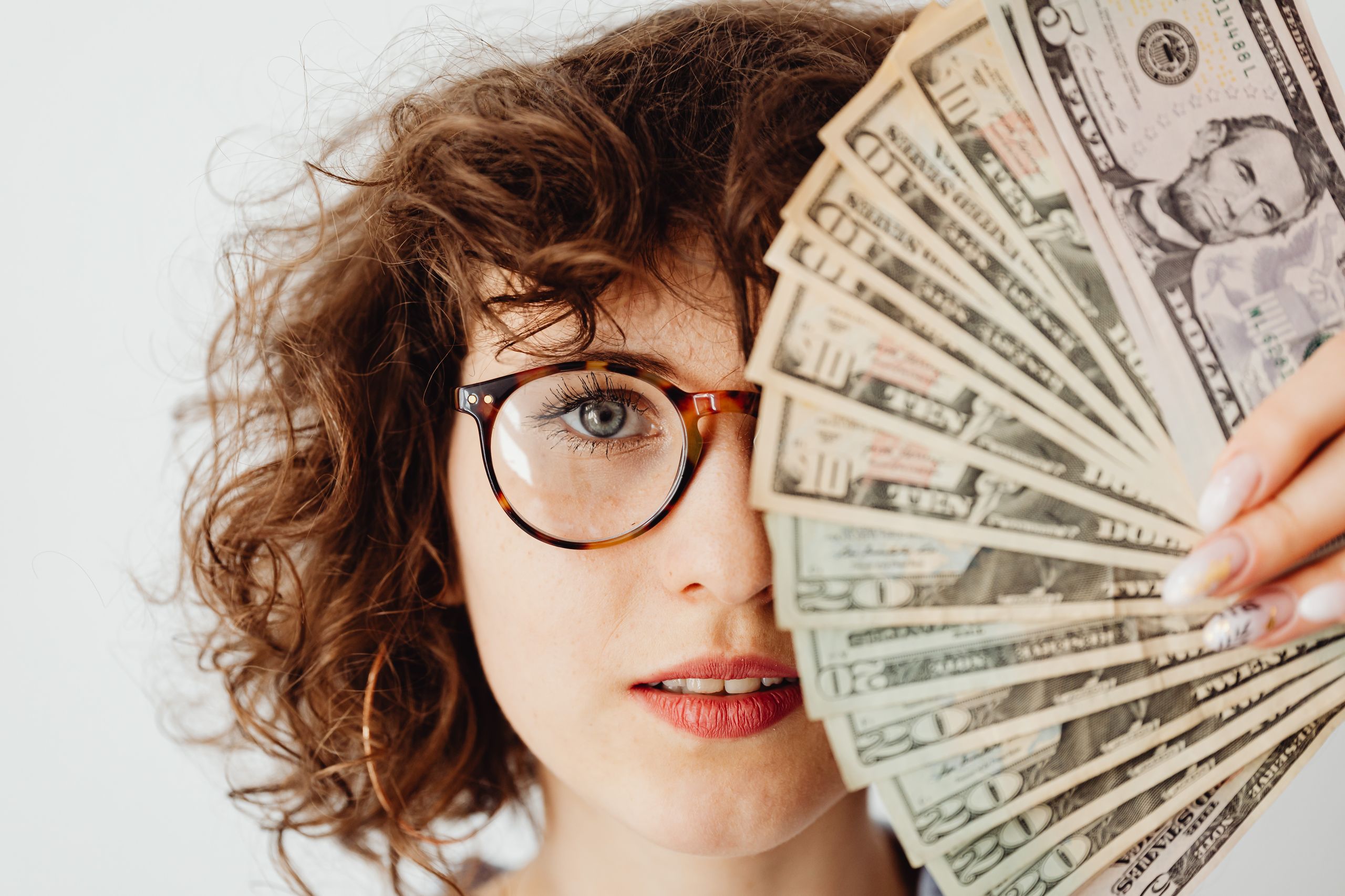 Caucasian woman with eyeglasses holding US dollar bills, to signify a paycheck being higher for london weighting
