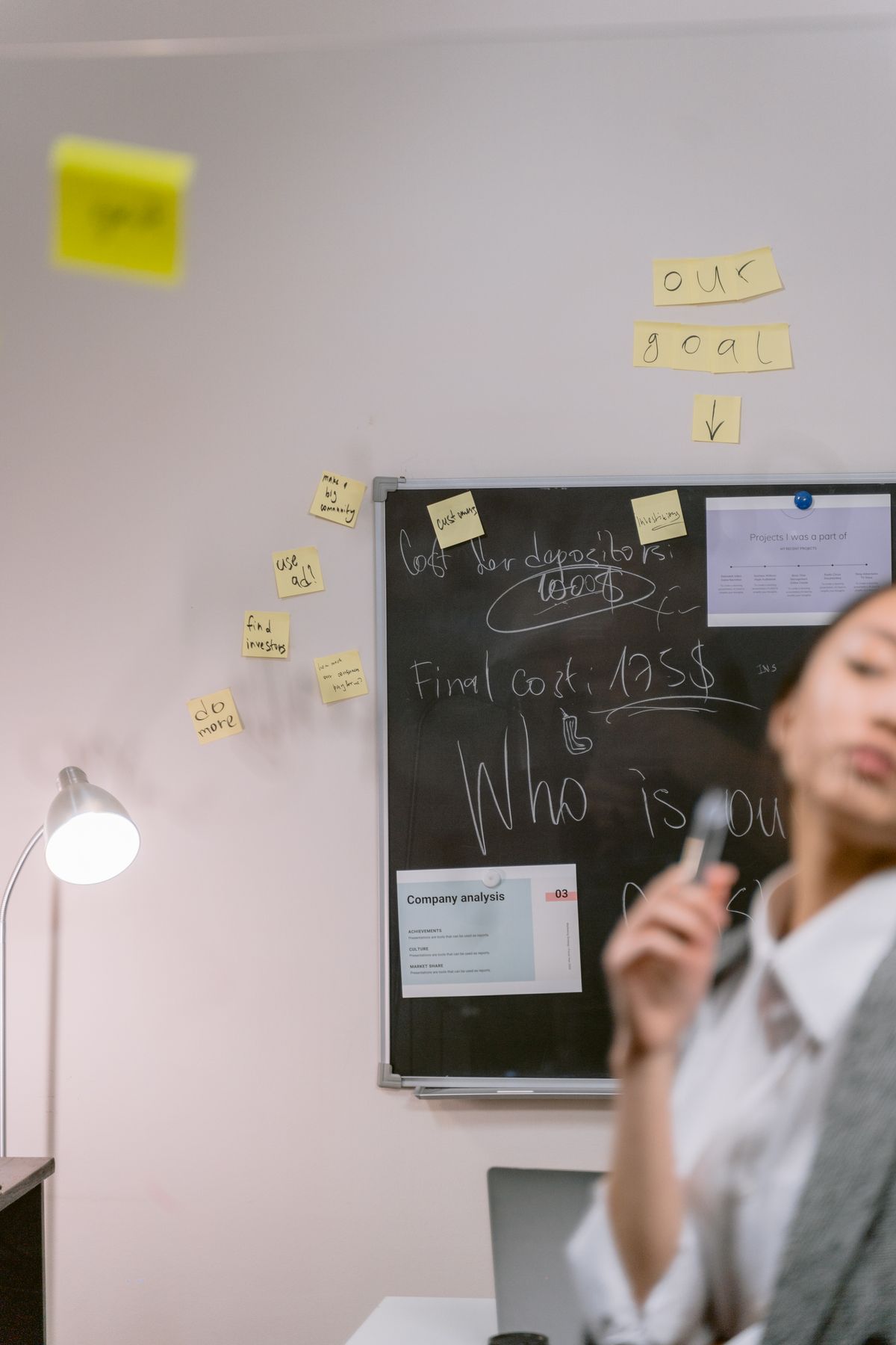 Chalkboard on a white wall with sticky notes and papers pinned beside it