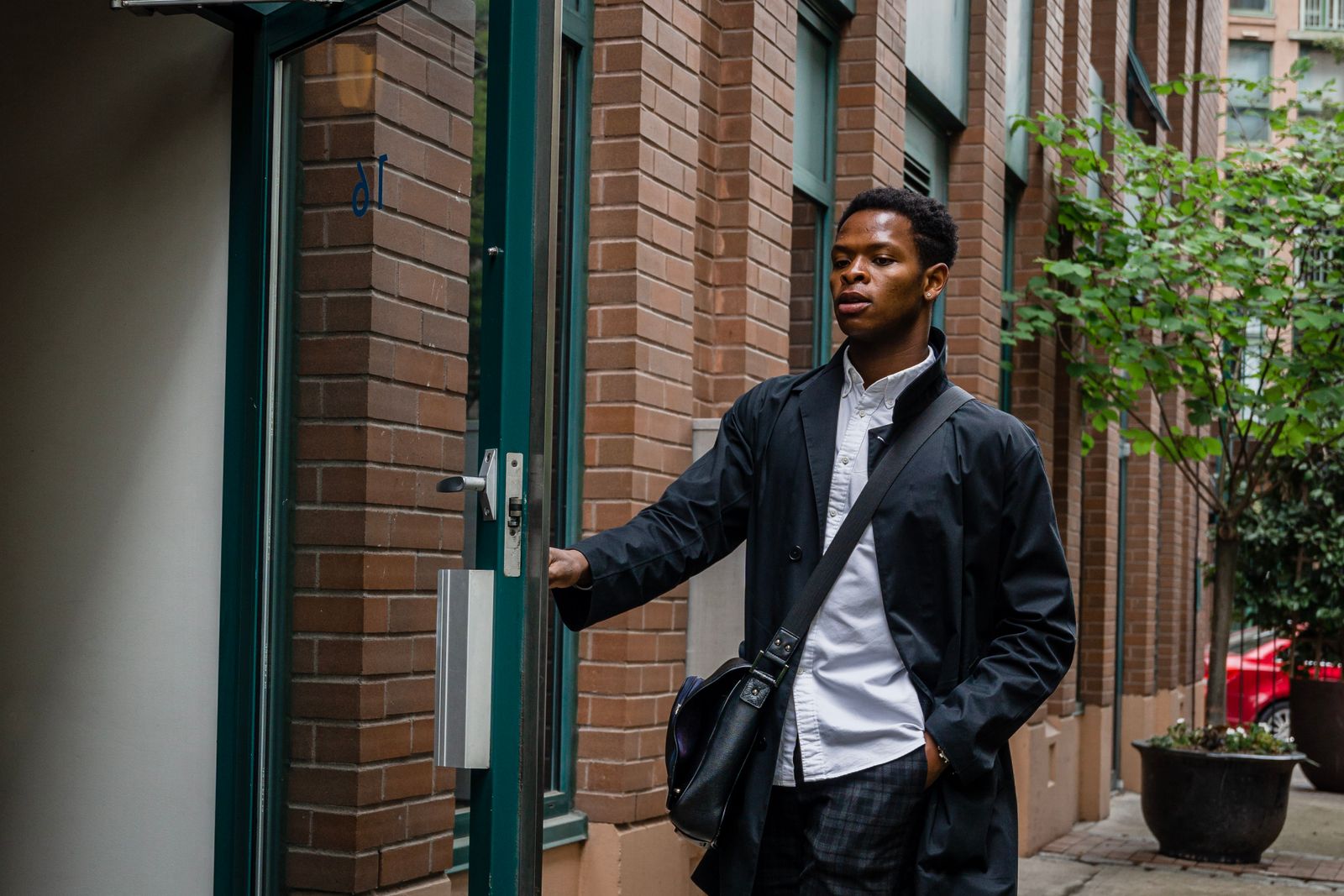 Young man in a coat opening a door to enter an office building, returning to work after mental health leave