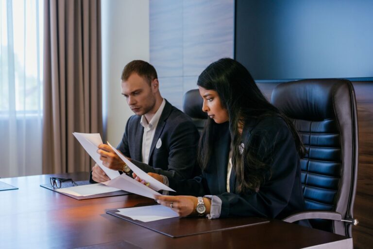Two colleagues sitting at a boardroom table reading through paper documents