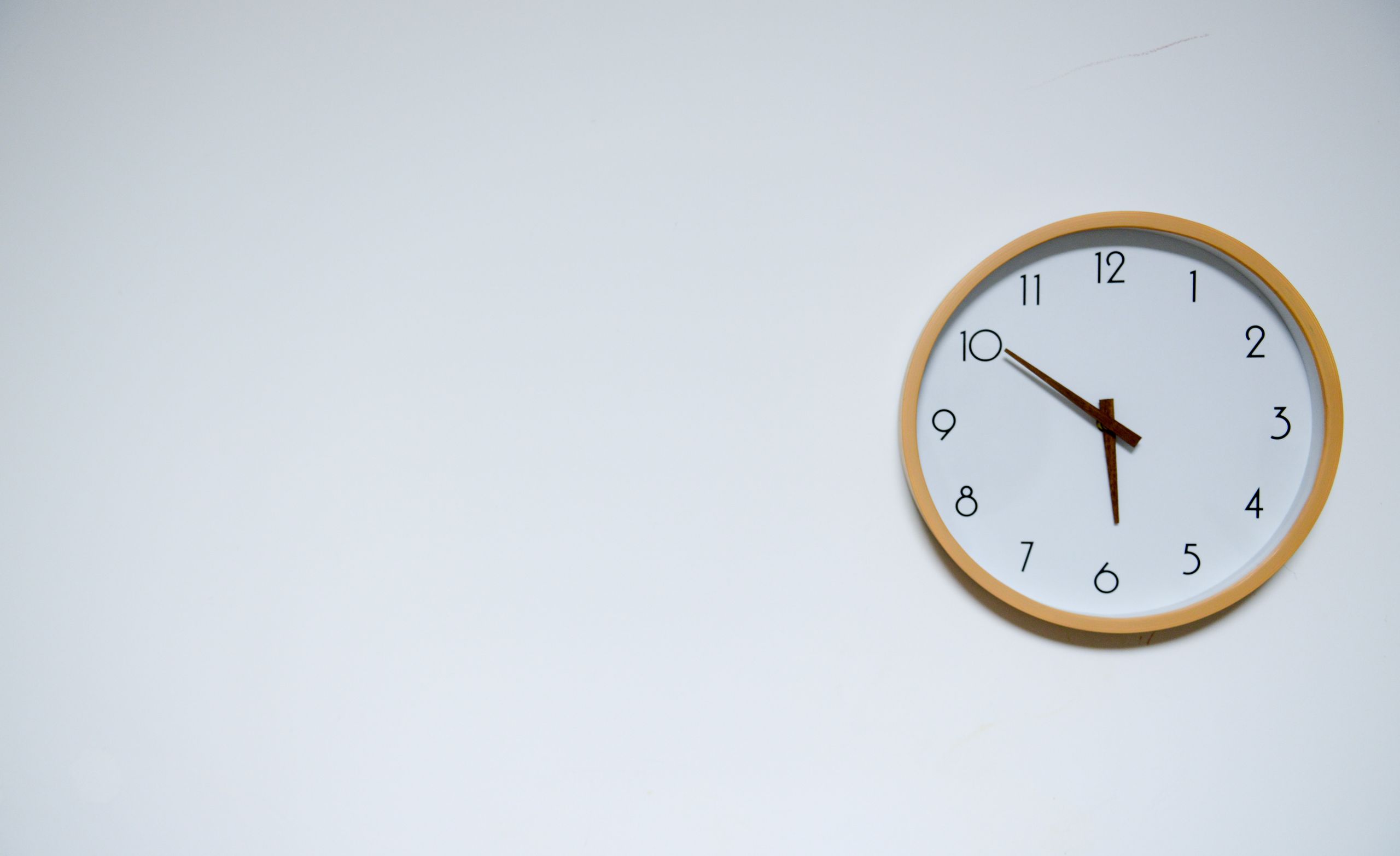 Simple wall clock with wooden frame against a white background, showing the time 10:10.