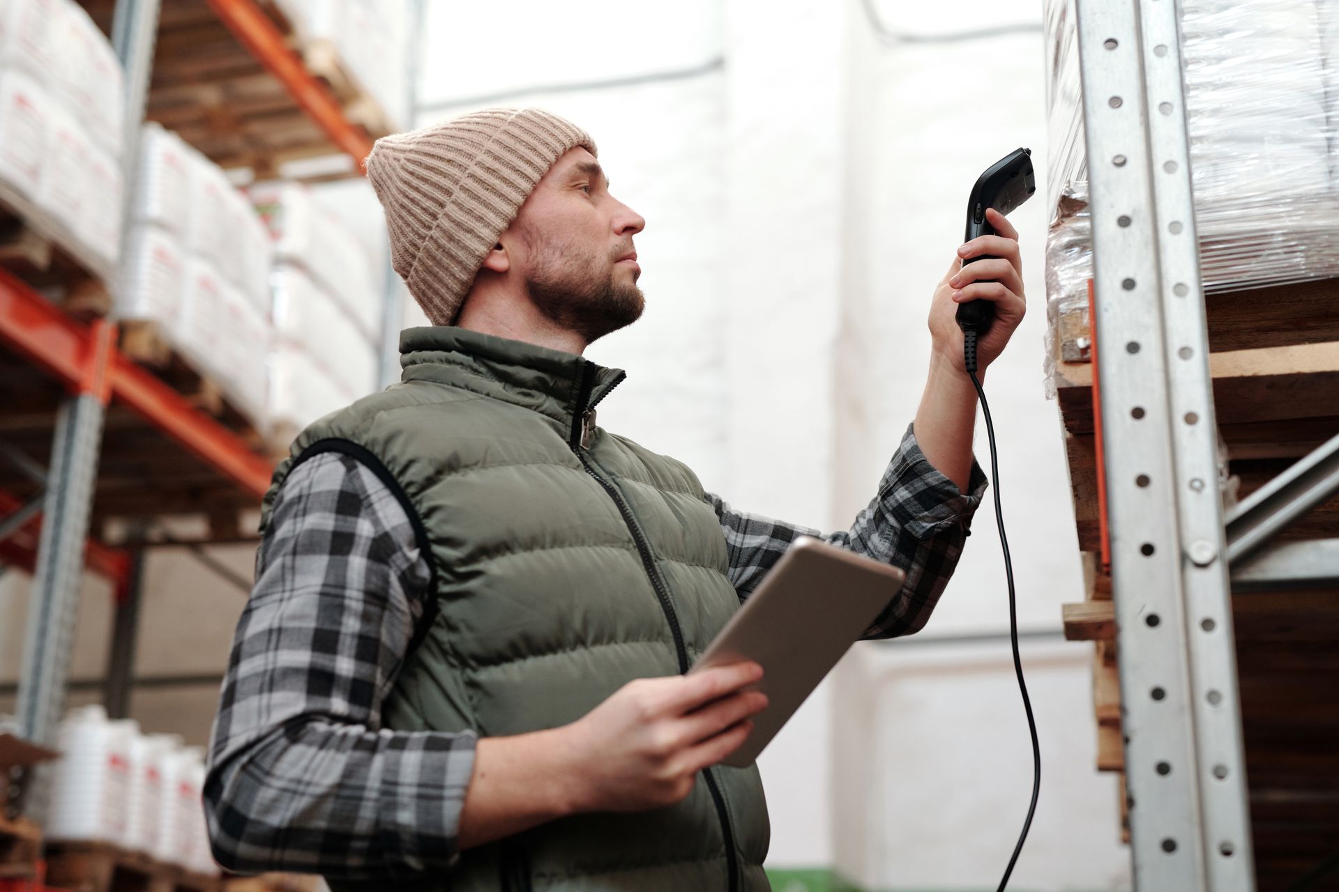 A warehouse worker holding a handheld scanner and a tablet beside tall storage shelves