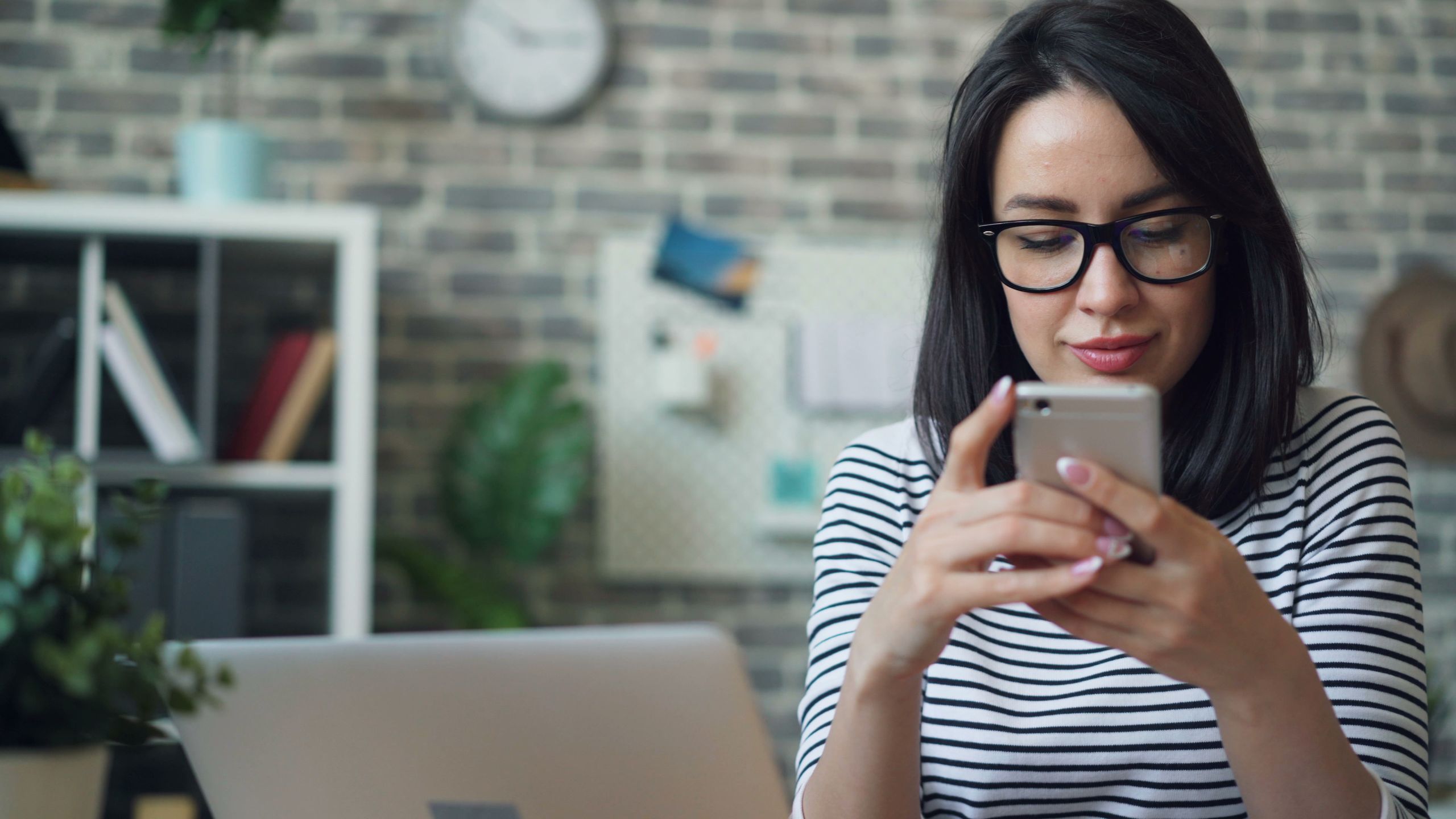 Young woman with eyeglasses using smartphone in a stylish office setting.